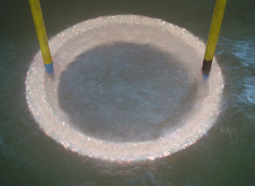 Metal part immersed in electrolyte during plasma electrolytic oxidation, its surface covered in small orange discharges