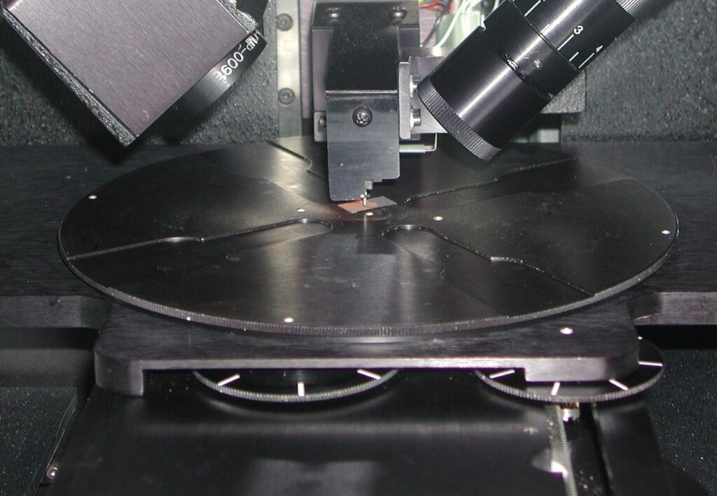 Stylus of a contact profilometer touching a small sample on the instrument stage